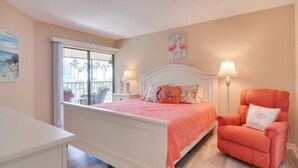 A bedroom with a white bed, a pink chair, and a view of palm trees through a window. - Walk to Bradenton Beach: Gulf-view Home w/ Lanai (Bradenton Beach)