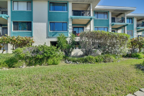 A multi-story hotel with balconies, a well-maintained lawn, and various shrubs.
