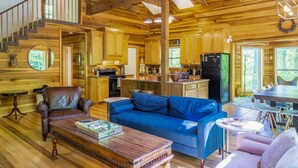 A wooden cabin interior with a living room, kitchen, and dining area.