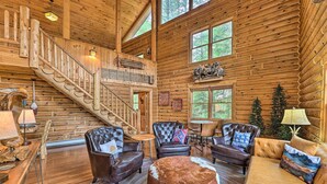 A log cabin interior with a staircase, leather furniture, and a large wooden dining table.