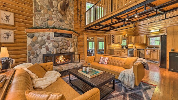 A log cabin interior with a stone fireplace, a sofa, and a dining area.
