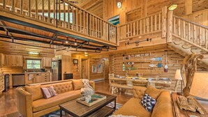 A spacious log cabin interior with a dining area, kitchen, and a loft bedroom.
