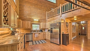 A spacious log cabin kitchen with wooden cabinets, a stainless steel refrigerator, and a large island.
