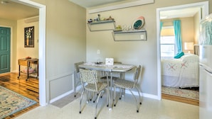 A dining area with a table and chairs, a wall-mounted shelf with dishes, and a door leading to another room.