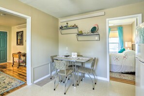 A dining area with a table and chairs, a wall-mounted shelf with dishes, and a door leading to another room.