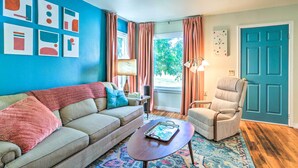 A living room with a blue wall, a beige sofa, a patterned rug, a wooden coffee table, and a teal door. - Modern Rapid City Duplex < 10 Mi to Natl Forest! (Rapid City)