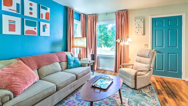 A living room with a blue wall, a beige sofa, a patterned rug, a wooden coffee table, and a teal door.