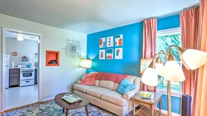 A living room with a sofa, coffee table, and a lamp. There is a kitchen area visible through an open door. - Modern Rapid City Duplex < 10 Mi to Natl Forest! (Rapid City)