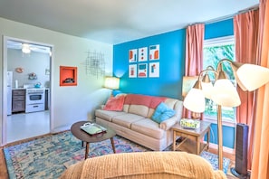 A living room with a sofa, coffee table, and a lamp. There is a kitchen area visible through an open door. - Modern Rapid City Duplex < 10 Mi to Natl Forest! (Rapid City)