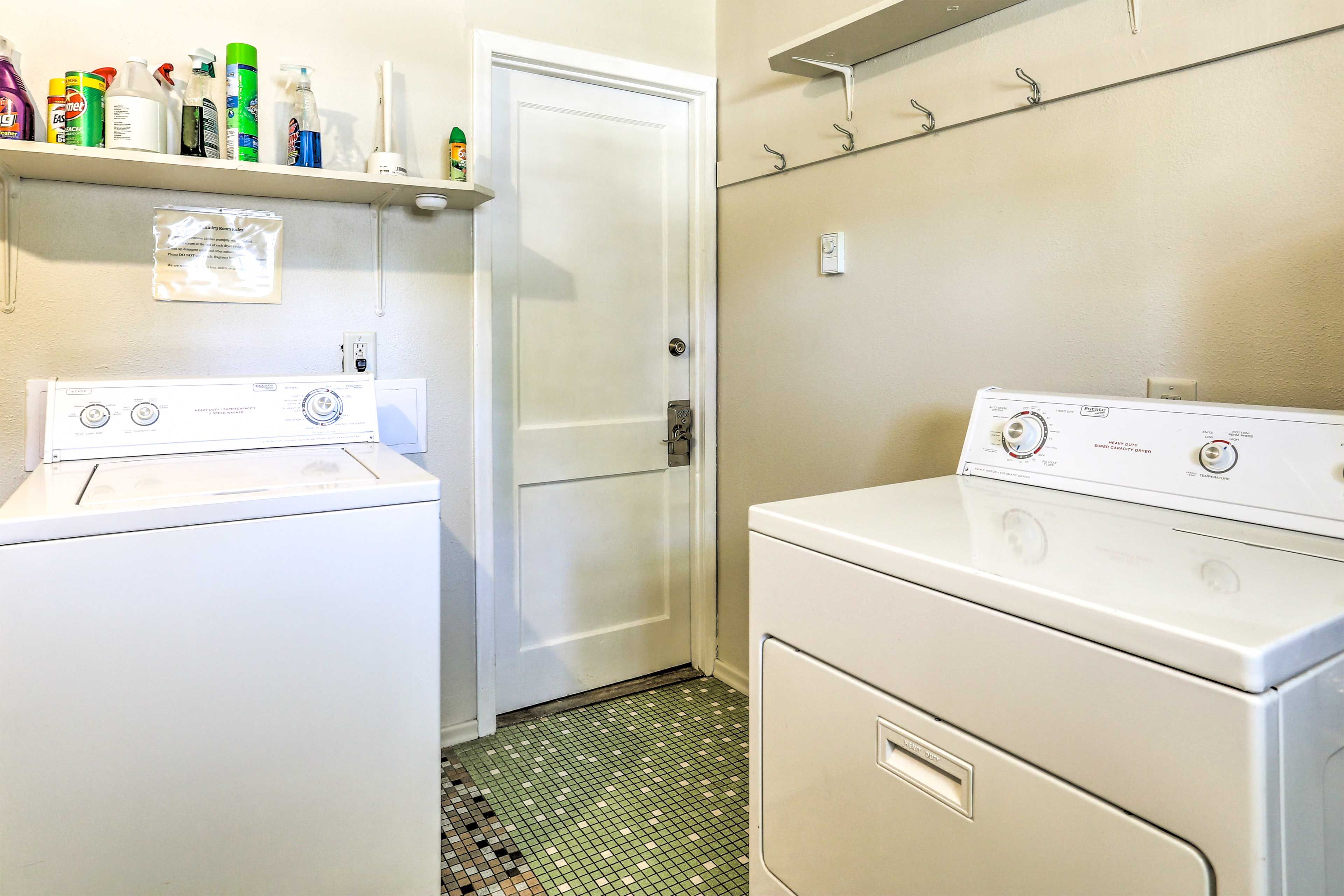 A laundry room with two washing machines, a shelf with cleaning supplies, and a door leading to another room.