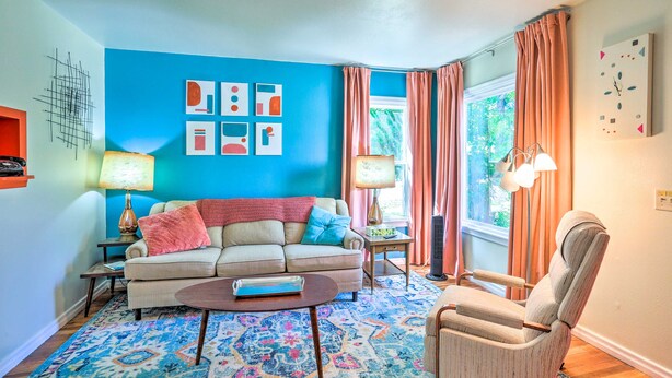 A living room with a blue wall, a beige sofa, a patterned rug, and a window with curtains. - Modern Rapid City Duplex < 10 Mi to Natl Forest! (Rapid City)