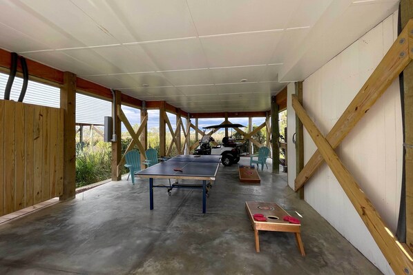 Un espacio al aire libre cubierto con una mesa de ping pong, una pequeña mesa con un juego de mesa y una motocicleta al fondo.