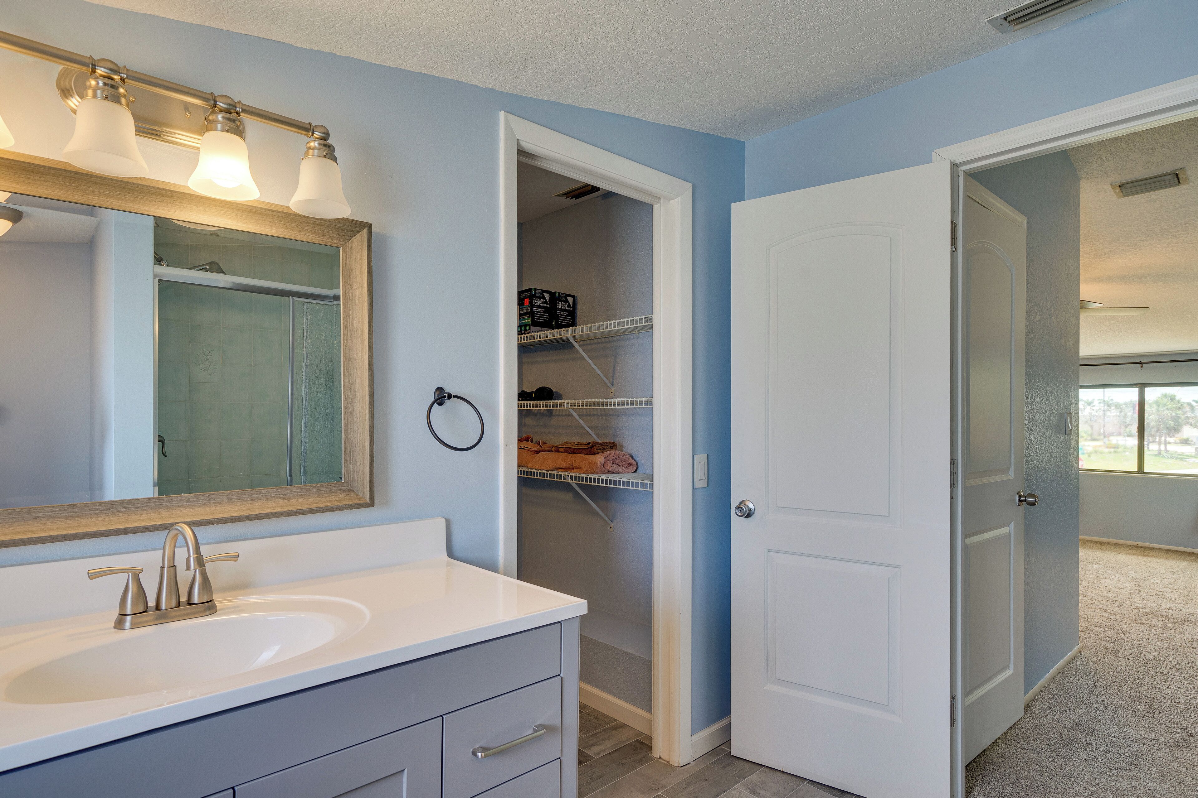 A bathroom with a white sink, a mirror, and a towel rack. There is a door leading to a closet with shelves.
