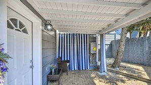 A covered patio area with a white door, a wicker chair, and a striped curtain. - Cute Central Placerville Studio: Pet Friendly (Placerville)