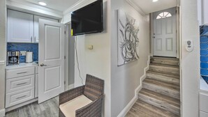 A modern kitchen with white cabinets, a flat-screen TV, and a wicker chair. - Cute Central Placerville Studio: Pet Friendly (Placerville)