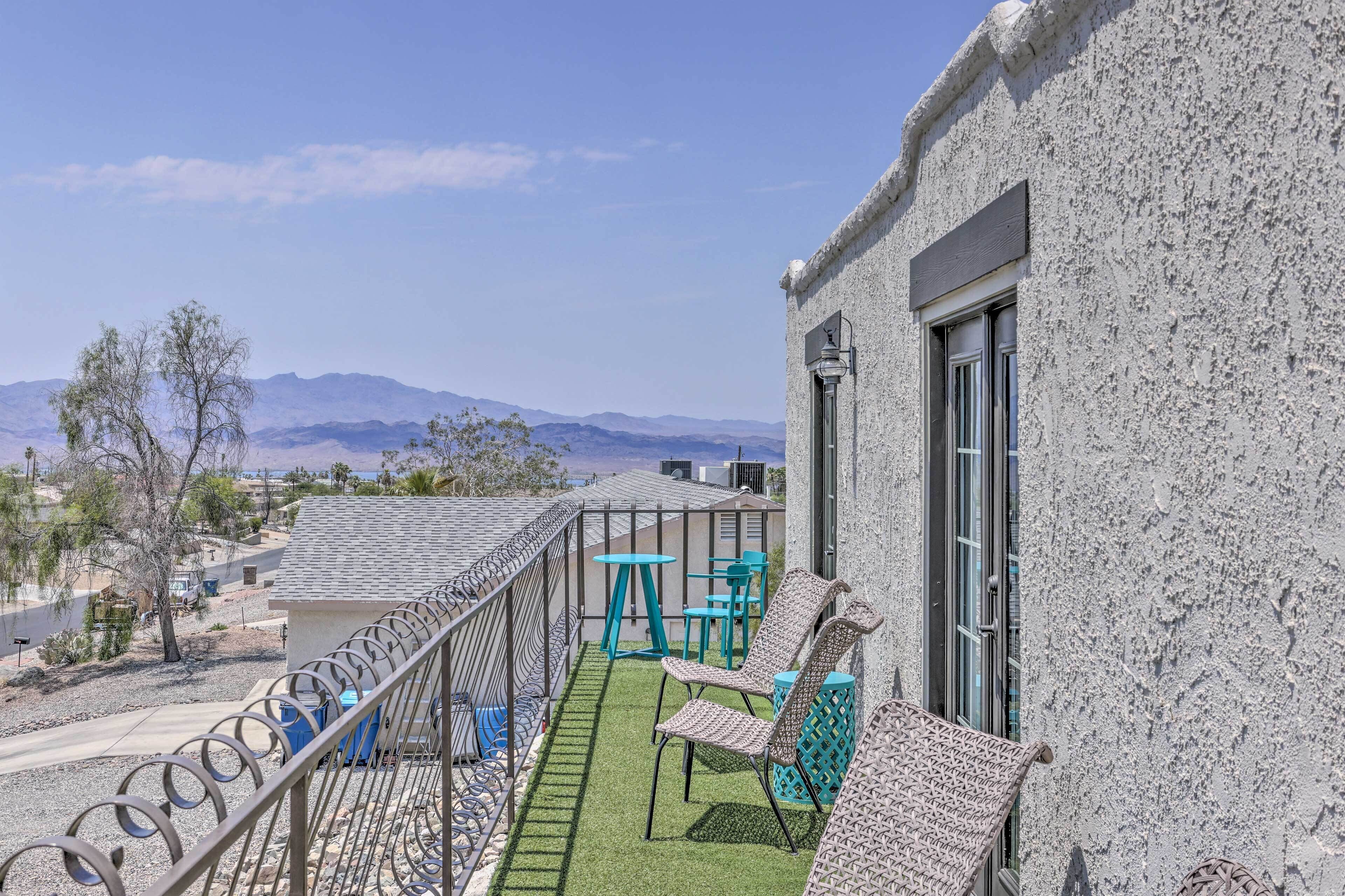 A balcony with a view of mountains, a small table, and two chairs.