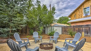 A backyard with four Adirondack chairs arranged in a circle around a fire pit, surrounded by gravel and trees. - Contemporary Boise House w/ Large Backyard! (Boise)