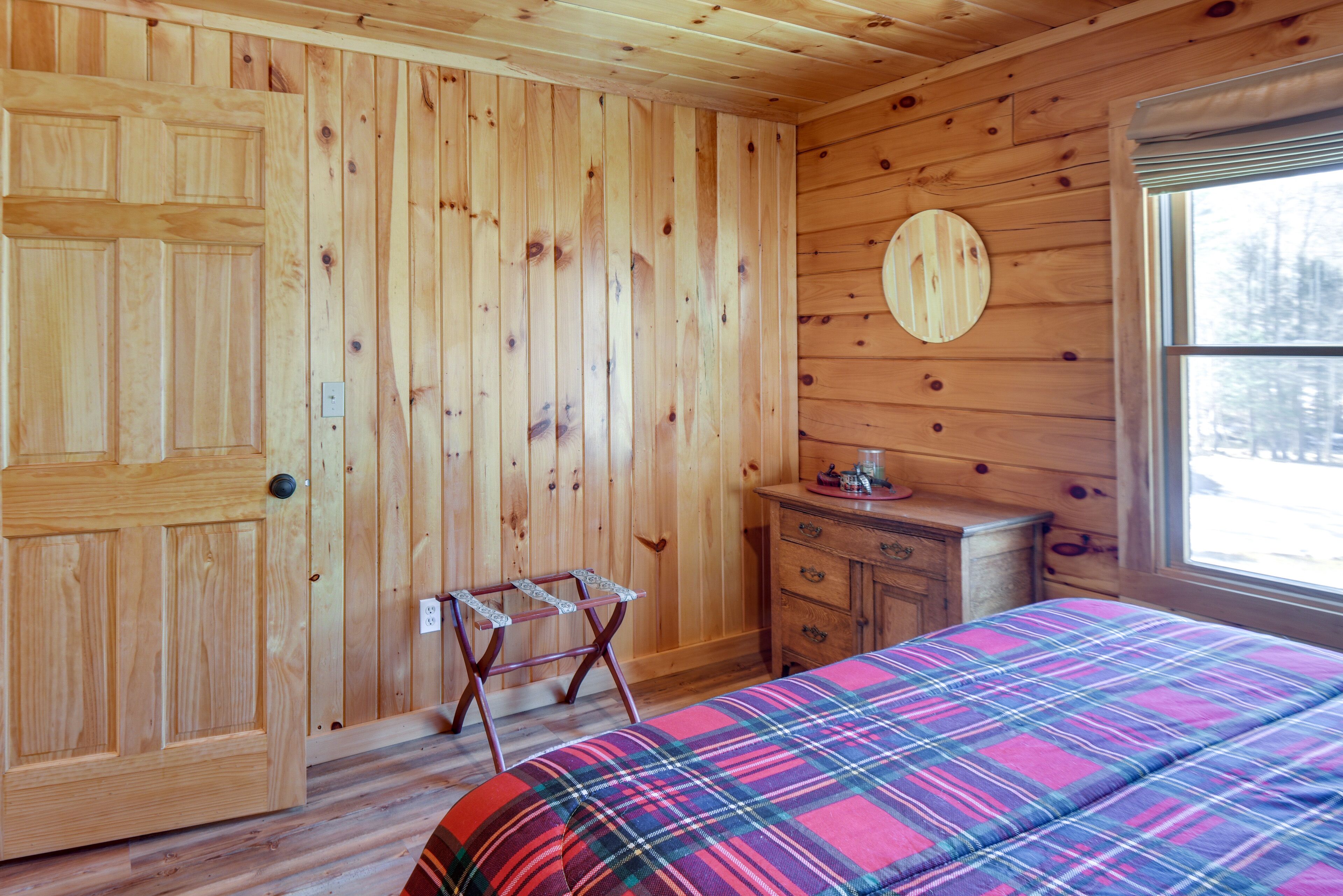 Quarto de madeira com uma cama, cômoda, espelho e porta.