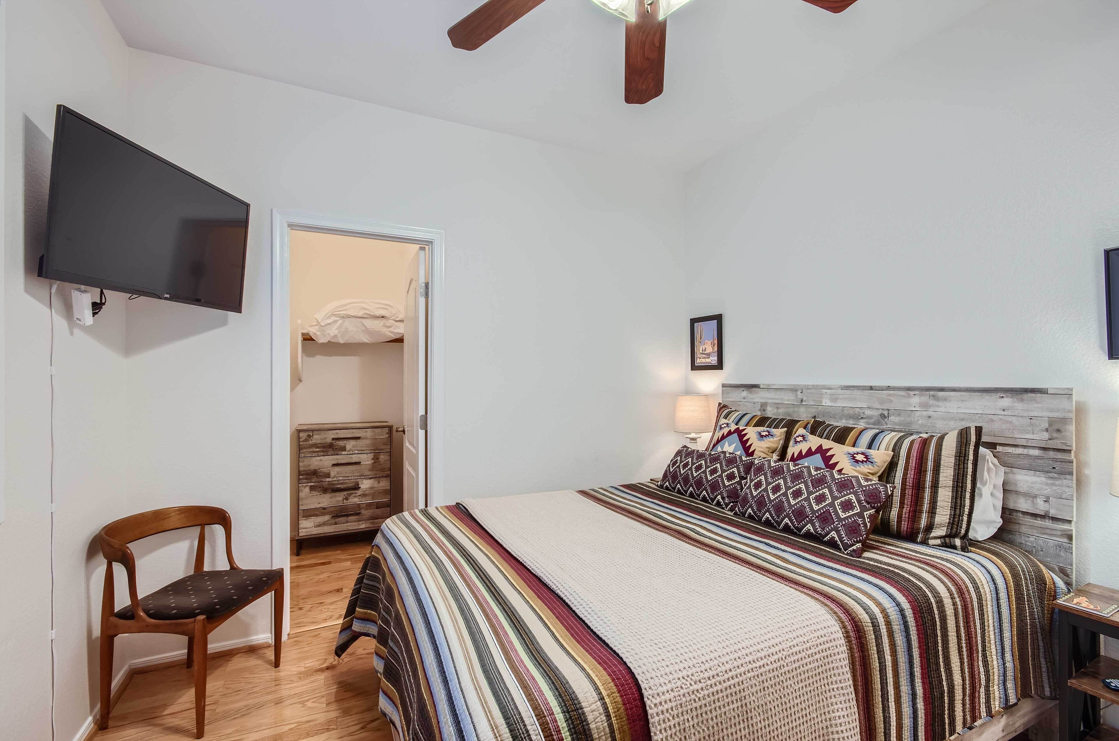 A bedroom with a bed, a TV, a wooden chair, and a door leading to another room.