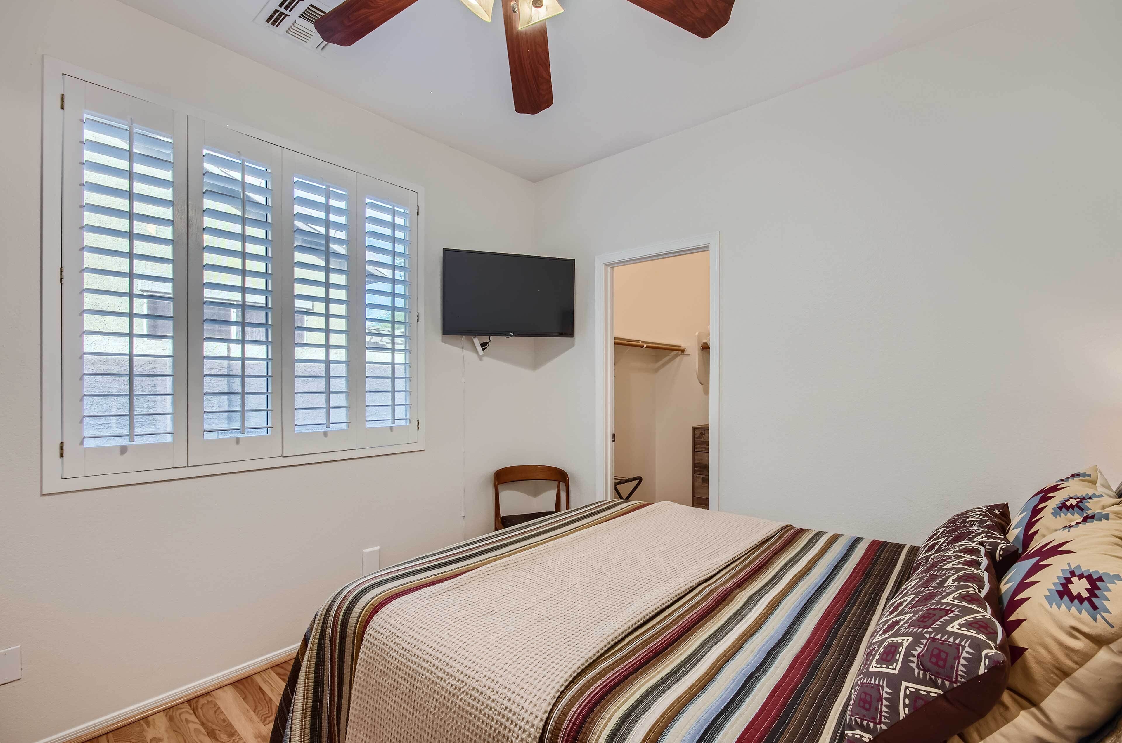 A bedroom with a bed, a TV mounted on the wall, and a window with blinds.