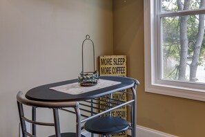 A small table with a metal frame and a blue cushioned chair. A sign with various words like "MORE SLEEP" and "MORE COFFEE" is visible in the background.
