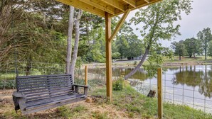Un banc en bois, placé sous une pergola, près d’un étang délimité par une clôture.