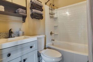 A bathroom with a white sink, toilet, and bathtub. There are towels on a rack and a shower caddy.