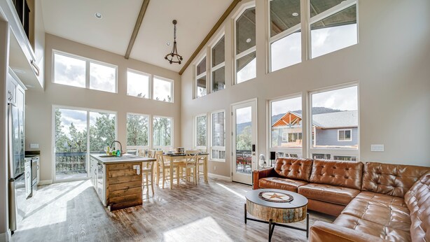 A spacious living area with a large leather sofa, a dining table with chairs, and a kitchen area with a wooden island. - Hot Tub + Deck: Mtn-view Pine Getaway! (Pine)