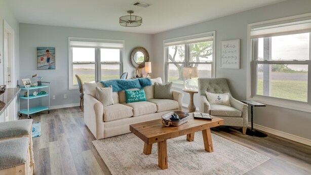 A living room with a beige sofa, a wooden coffee table, and a view of the outdoors through large windows. - Rockport Condo ~ 6 Mi to Rockport Beach Park! (Rockport)