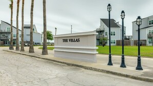 A sign labeled "THE VILLAS" with a row of palm trees and a paved walkway. - Rockport Condo ~ 6 Mi to Rockport Beach Park! (Rockport)