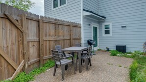 A patio area with a table and chairs, a wooden fence, and a house with a green door. - Rockport Condo ~ 6 Mi to Rockport Beach Park! (Rockport)