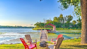 A lakeside deck with Adirondack chairs and a fire pit, leading to a dock and a covered area. - Waterfront Mound Retreat w/ Dock & Lake Access! (Mound)