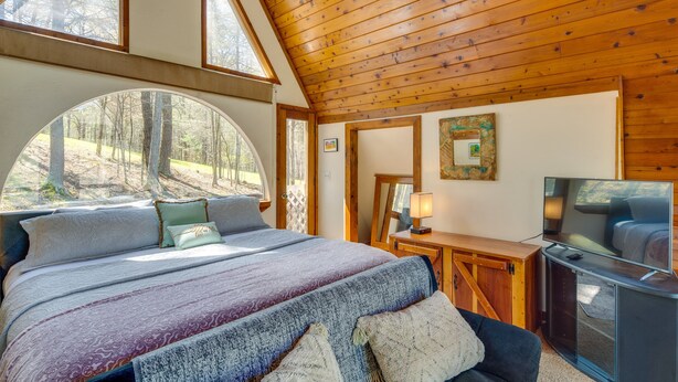 Une chambre avec un grand lit, une télévision et une vue sur la forêt.