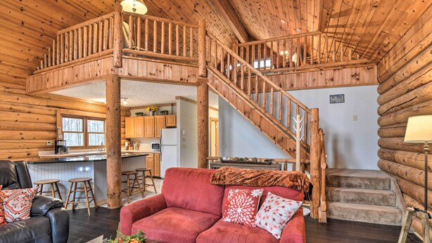 A log cabin interior with a red sofa, wooden staircase, and a kitchen area. - Secluded Gaylord Cabin w/ Deck, Fire Pit & Grill! (Gaylord)