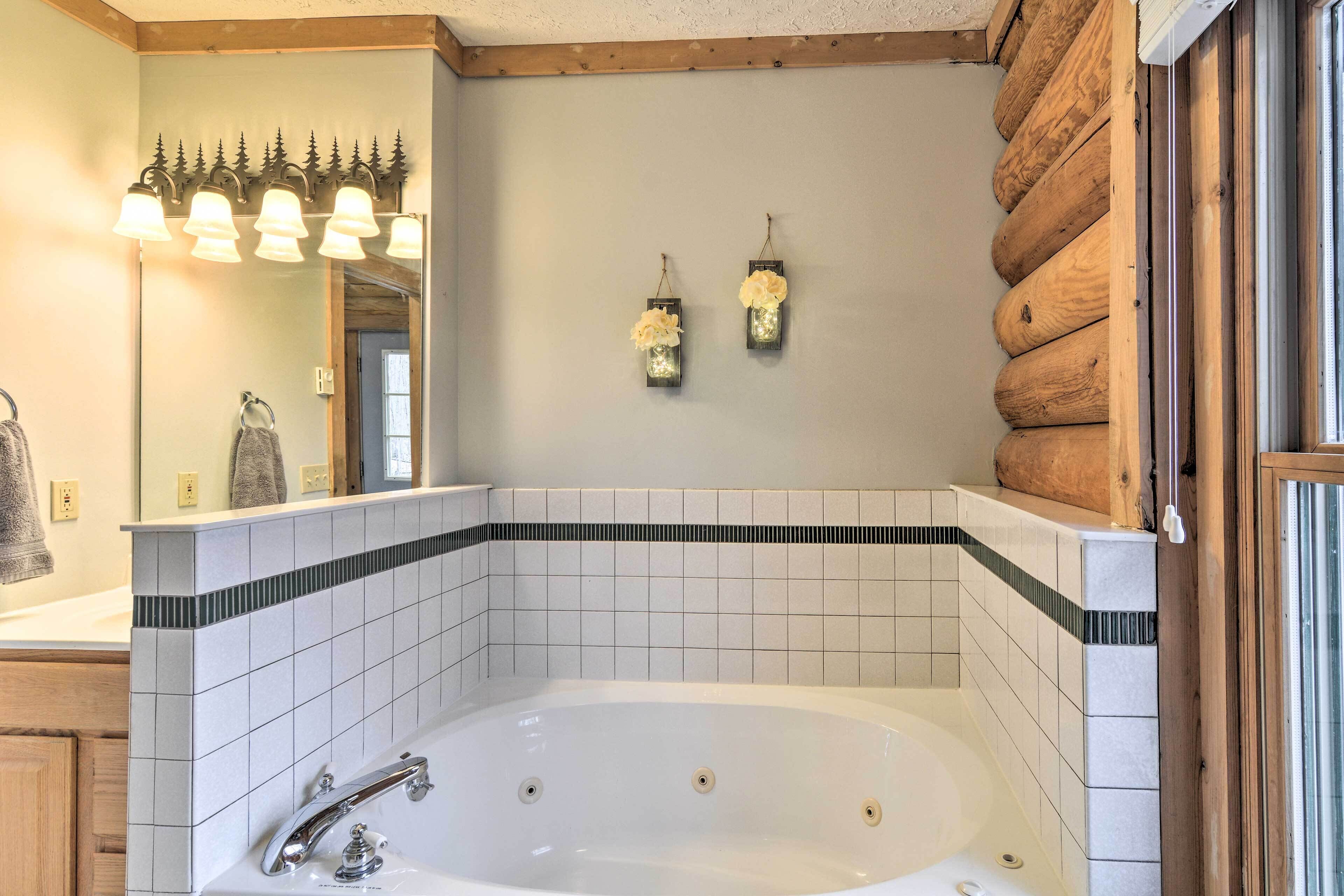 Une salle de bain dotée d’une grande baignoire, d’un mur en bois brut et de deux appliques murales.