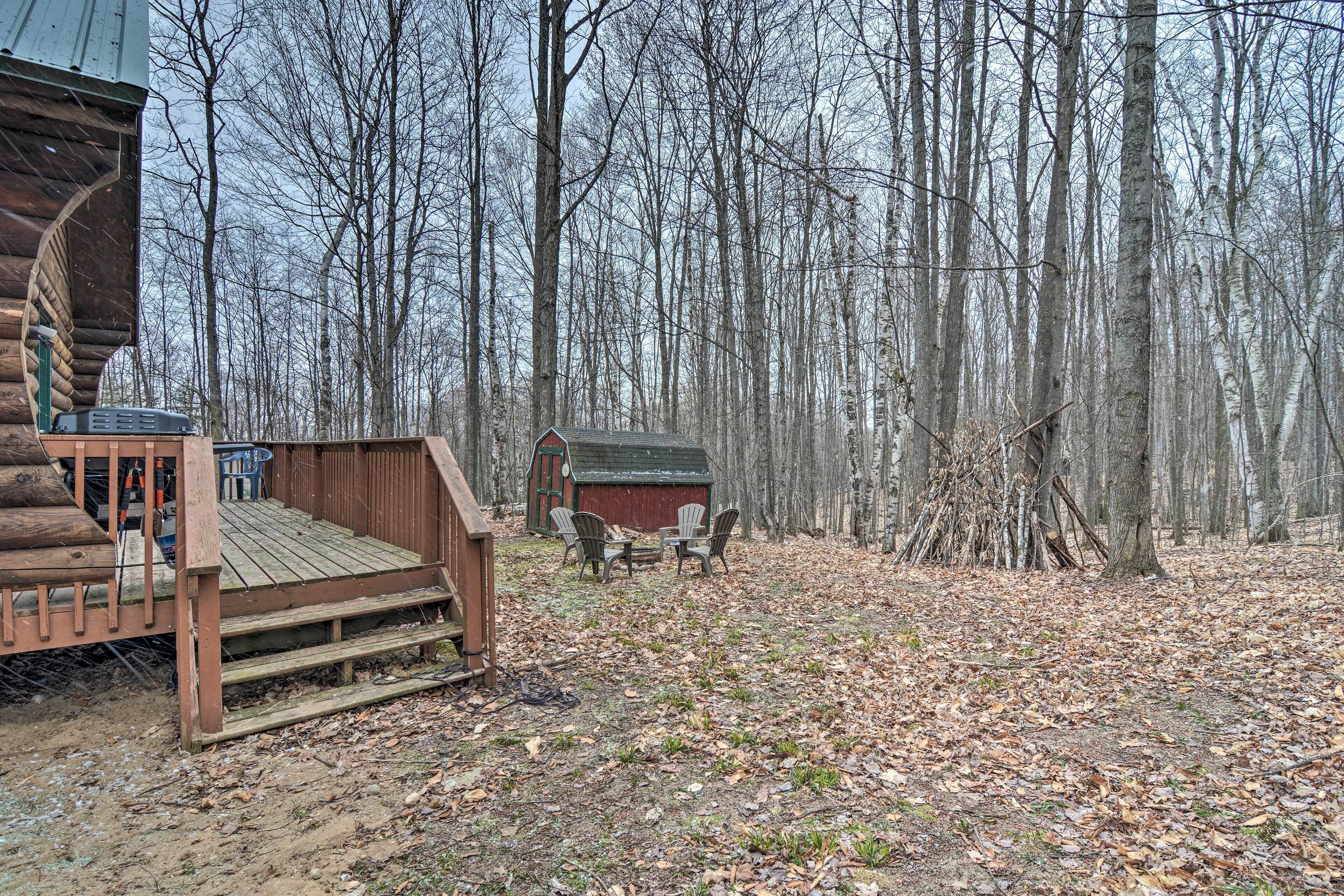 A cabin with a wooden deck and a small shed in a forested area.