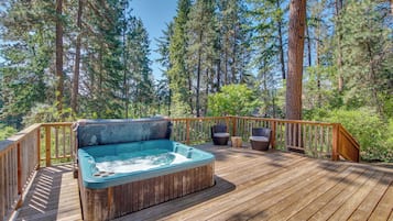 A wooden deck with a hot tub, surrounded by tall trees and a wooden railing.