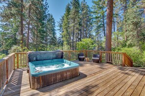 A wooden deck with a hot tub, surrounded by tall trees and a wooden railing.