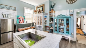 Una cocina con un refrigerador de acero inoxidable, una encimera de mármol, un lavamanos y un armario azul turquesa con puertas de vidrio.