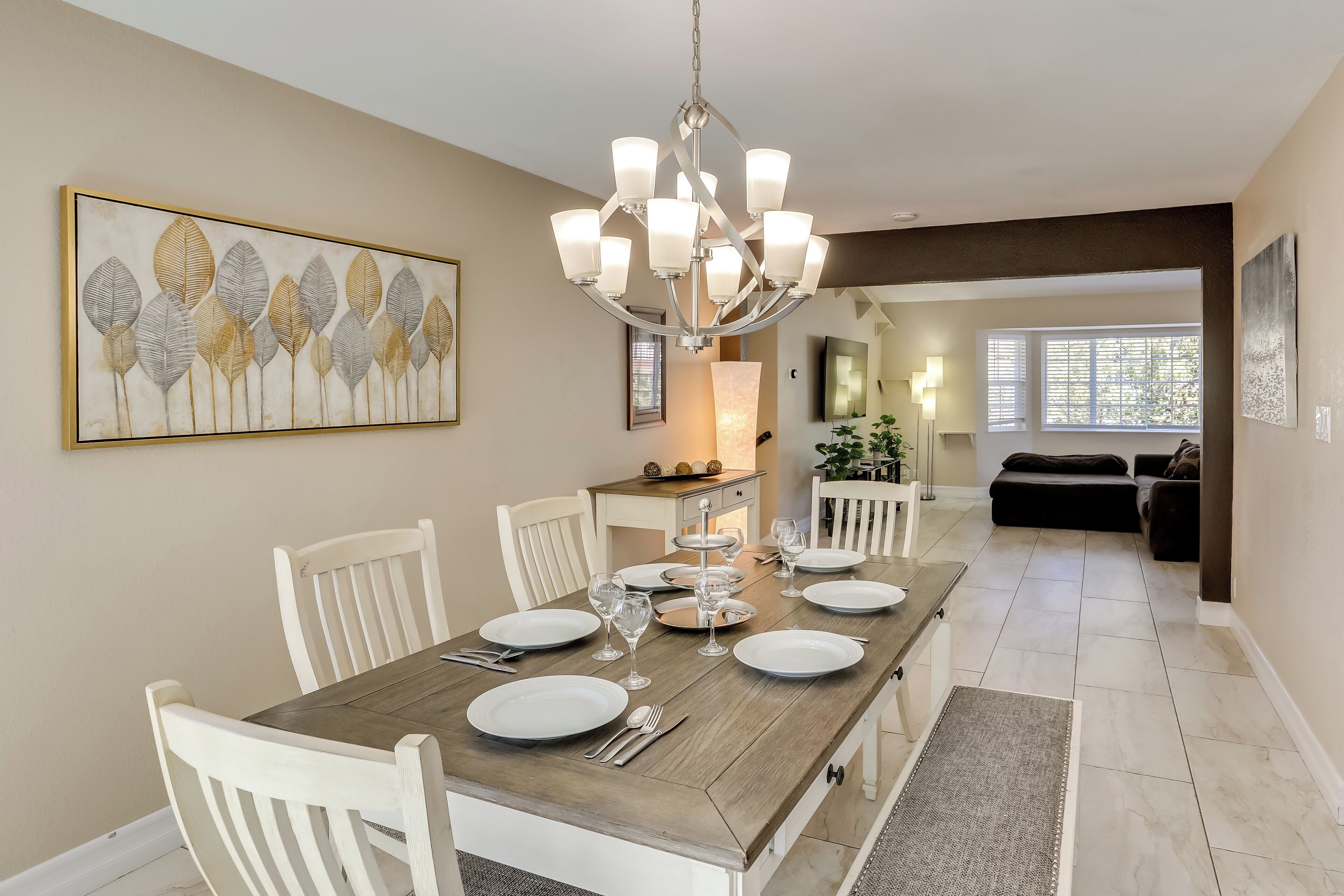Un coin repas avec une table en bois dressée pour six personnes, des chaises blanches et un lustre.