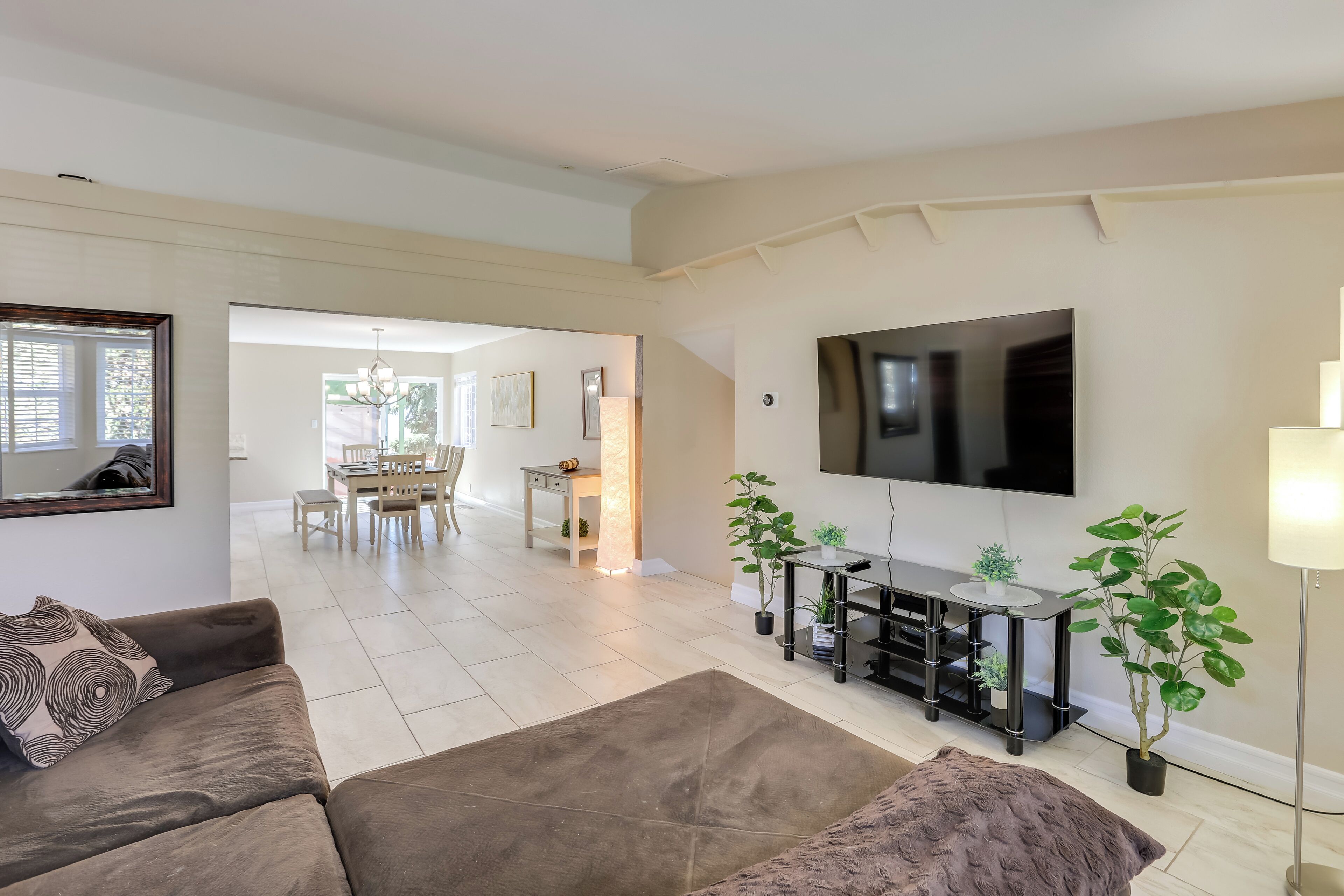 A modern living room with a flat-screen TV, a sofa, a coffee table, and a dining area in the background.