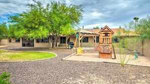 A playground with swings and a climbing structure, surrounded by a building with a sloped roof and a covered seating area. - Modern Glendale Desert Destination w/ Patio! (Glendale)