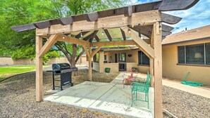 A covered outdoor area with a grill, concrete floor, and green metal chairs. - Modern Glendale Desert Destination w/ Patio! (Glendale)