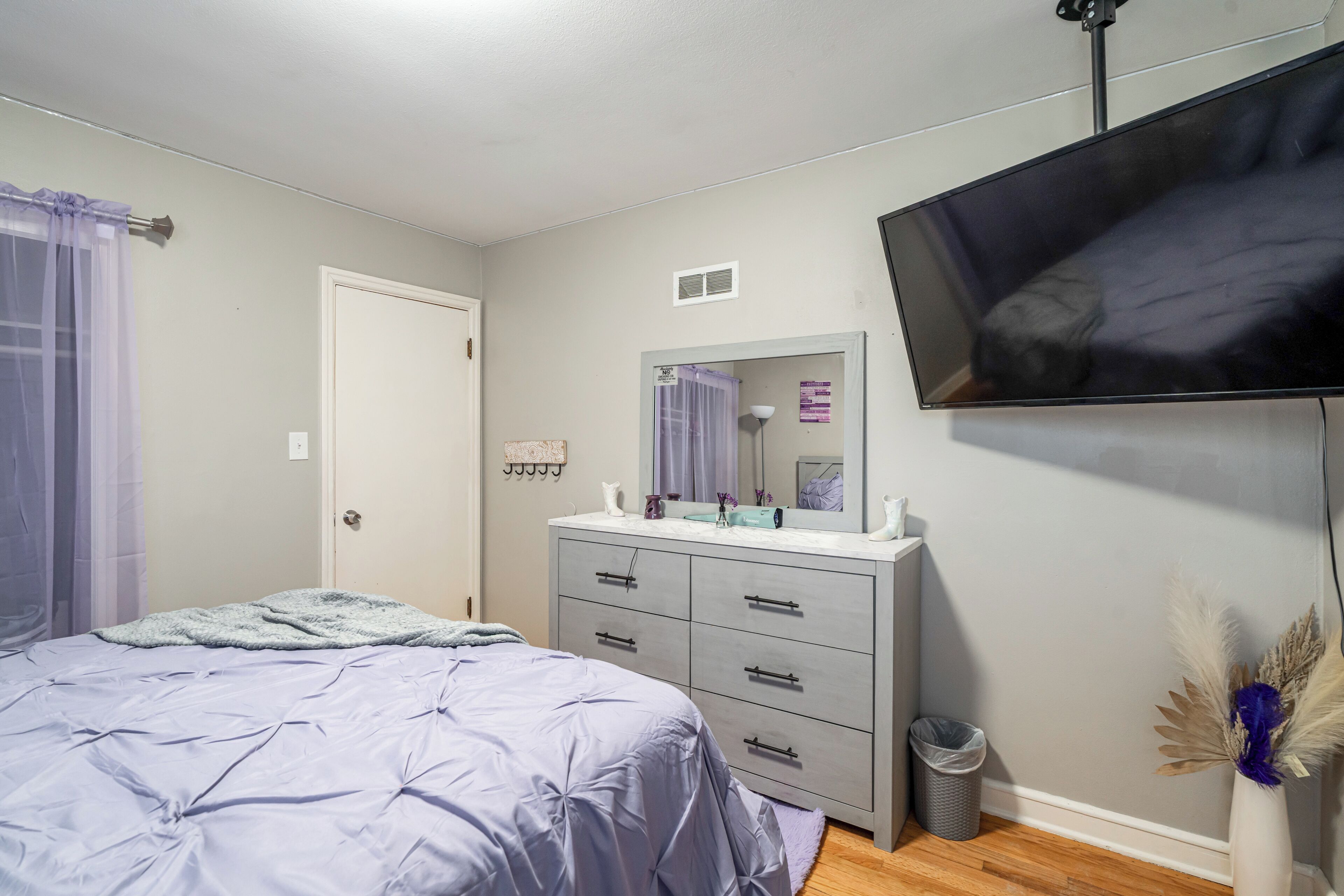 A bedroom with a bed, dresser, mirror, TV, and a trash can.