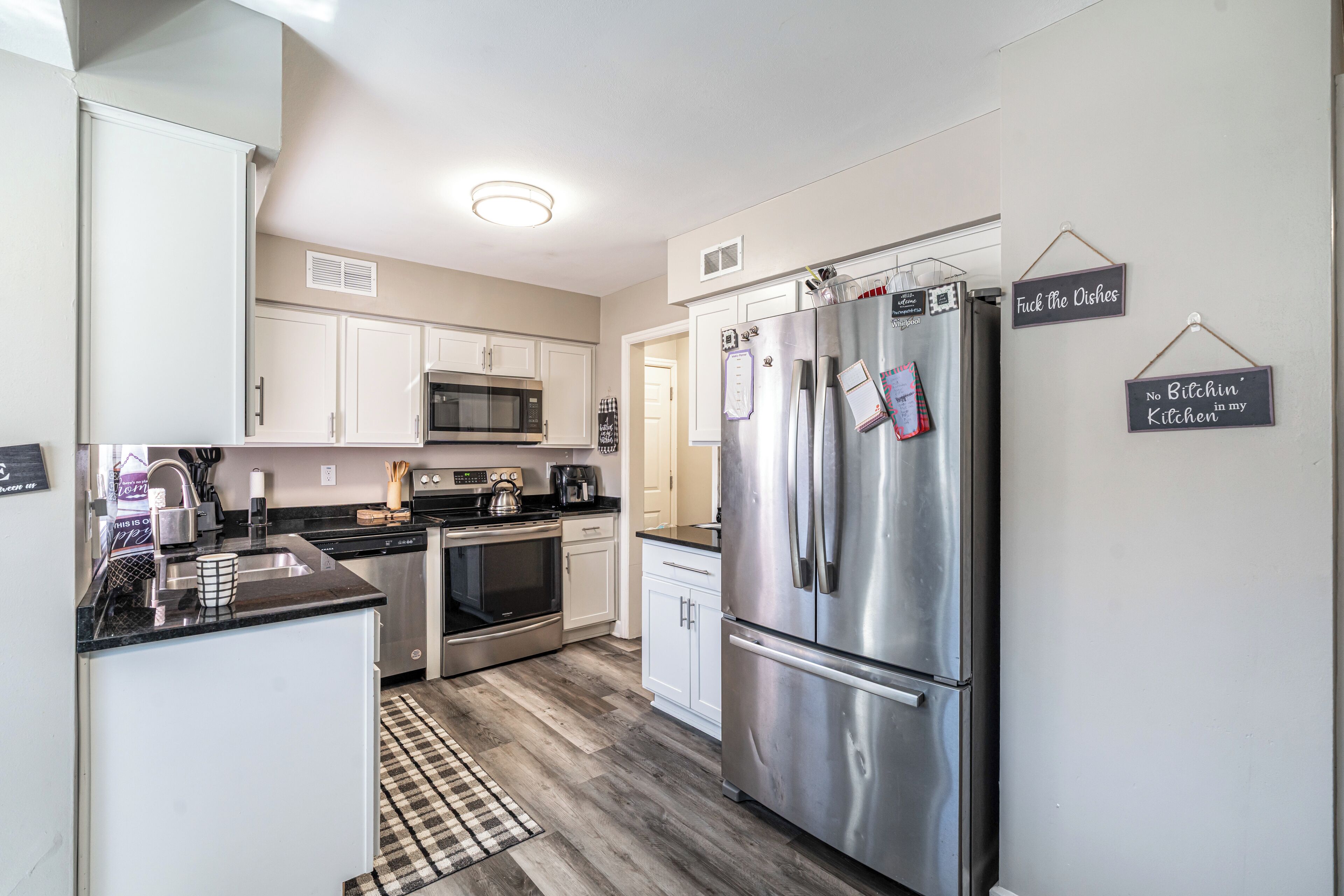 A modern kitchen with stainless steel appliances, white cabinetry, and a checkered rug.