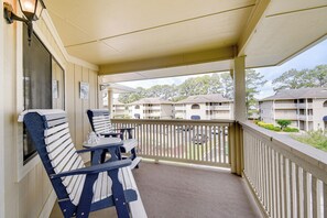 A balcony with two white and blue benches, a small table, and a view of a residential building with multiple balconies.