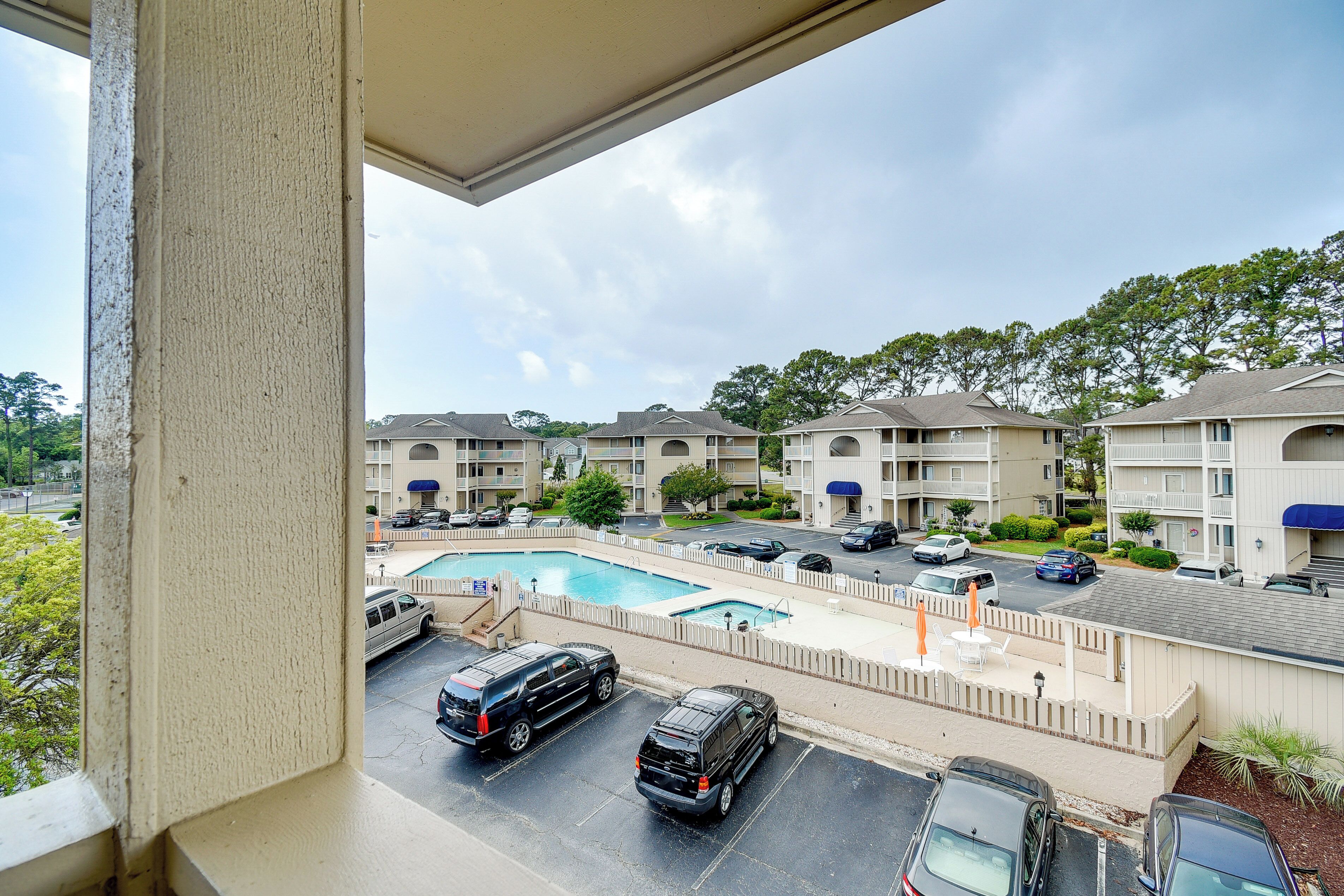 A view of a hotel with a swimming pool, multiple parking spaces, and a covered walkway.