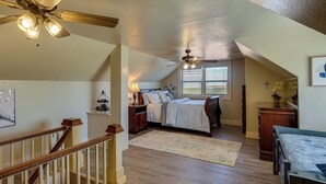 A bedroom with a bed, a desk, a chair, a window with blinds, a ceiling fan, and a staircase. - Lamesa Vacation Rental w/ Covered Patio & Fire Pit (Lamesa)