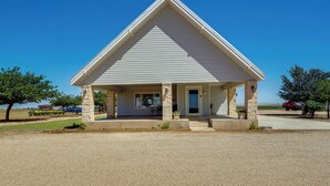A small, single-story building with a gabled roof and a front porch supported by stone pillars. - Lamesa Vacation Rental w/ Covered Patio & Fire Pit (Lamesa)
