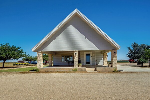 A small, single-story building with a gabled roof and a front porch supported by stone pillars. - Lamesa Vacation Rental w/ Covered Patio & Fire Pit (Lamesa)